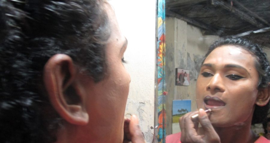 A transgnder woman applies her make-up in front of a mirror