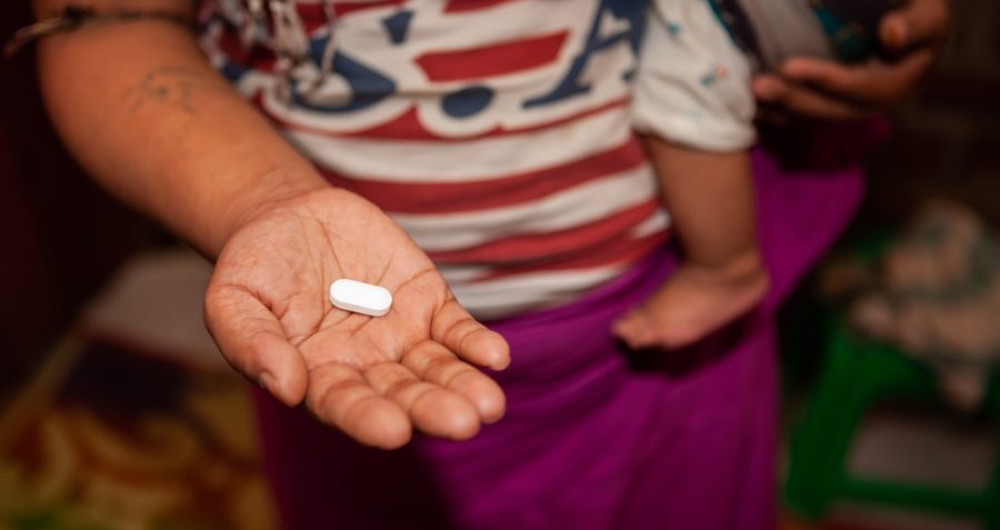 A mother holding her baby and holding her hand out containing an ARV pill