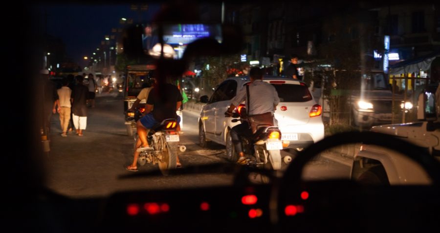 Motorbikes, pedestrians and cars on a busy nighttime road.
