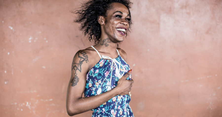 A transgender woman smiling and standing in front of a wall