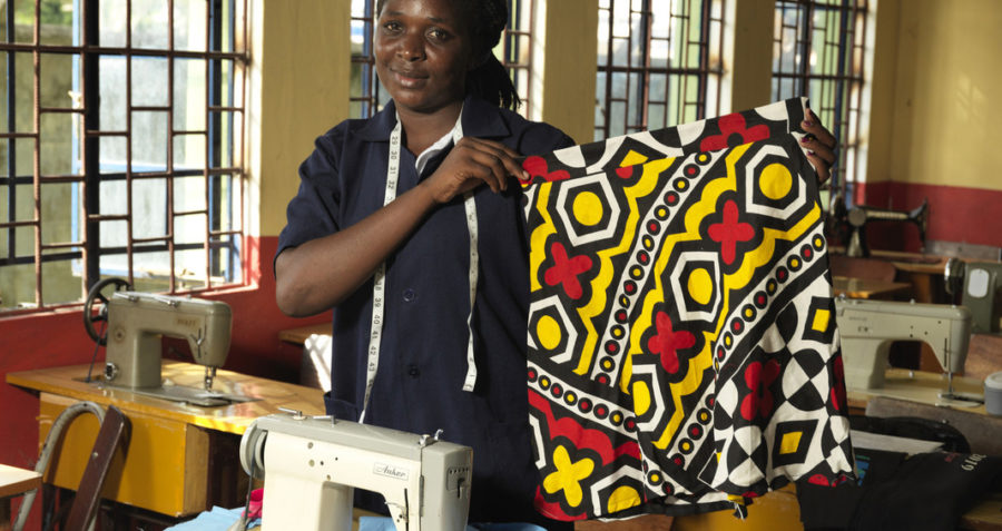 A young woman holds up a patterned skirt she has made standing by her sewing machine