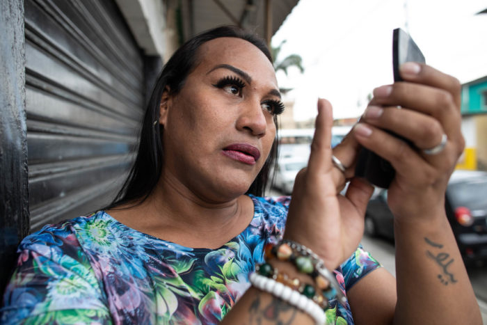 A transgender woman checks her make-up in a hand-mirror while standing on the street