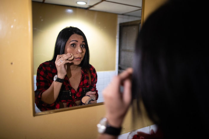 A transgender woman checks her make up in the bathroom mirror