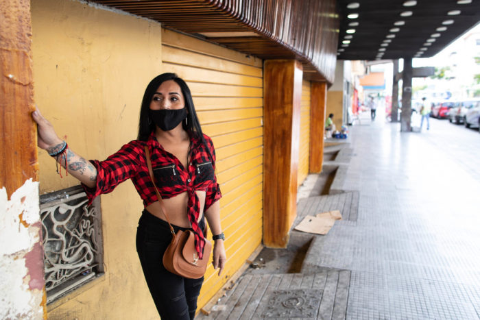 A transgender woman stands on the street wearing a face mask