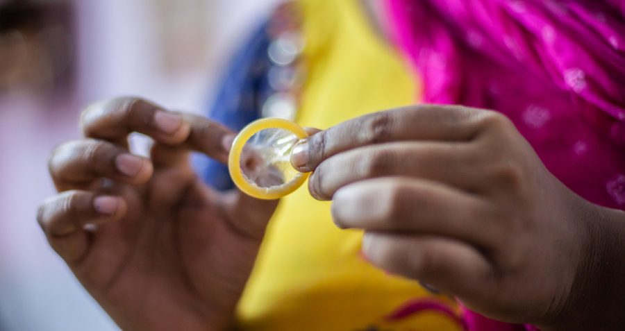 A woman wearing a pink, yellow and blue sari holds a condom