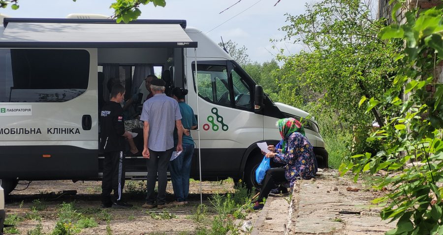 People stand and sit outside a van