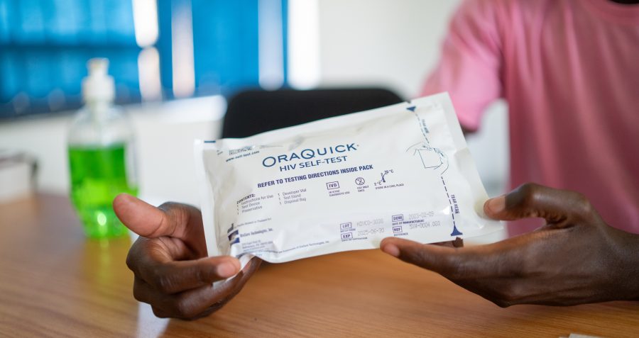 A person in a pink t-shirt holds a HIV self testing kit in its packaging