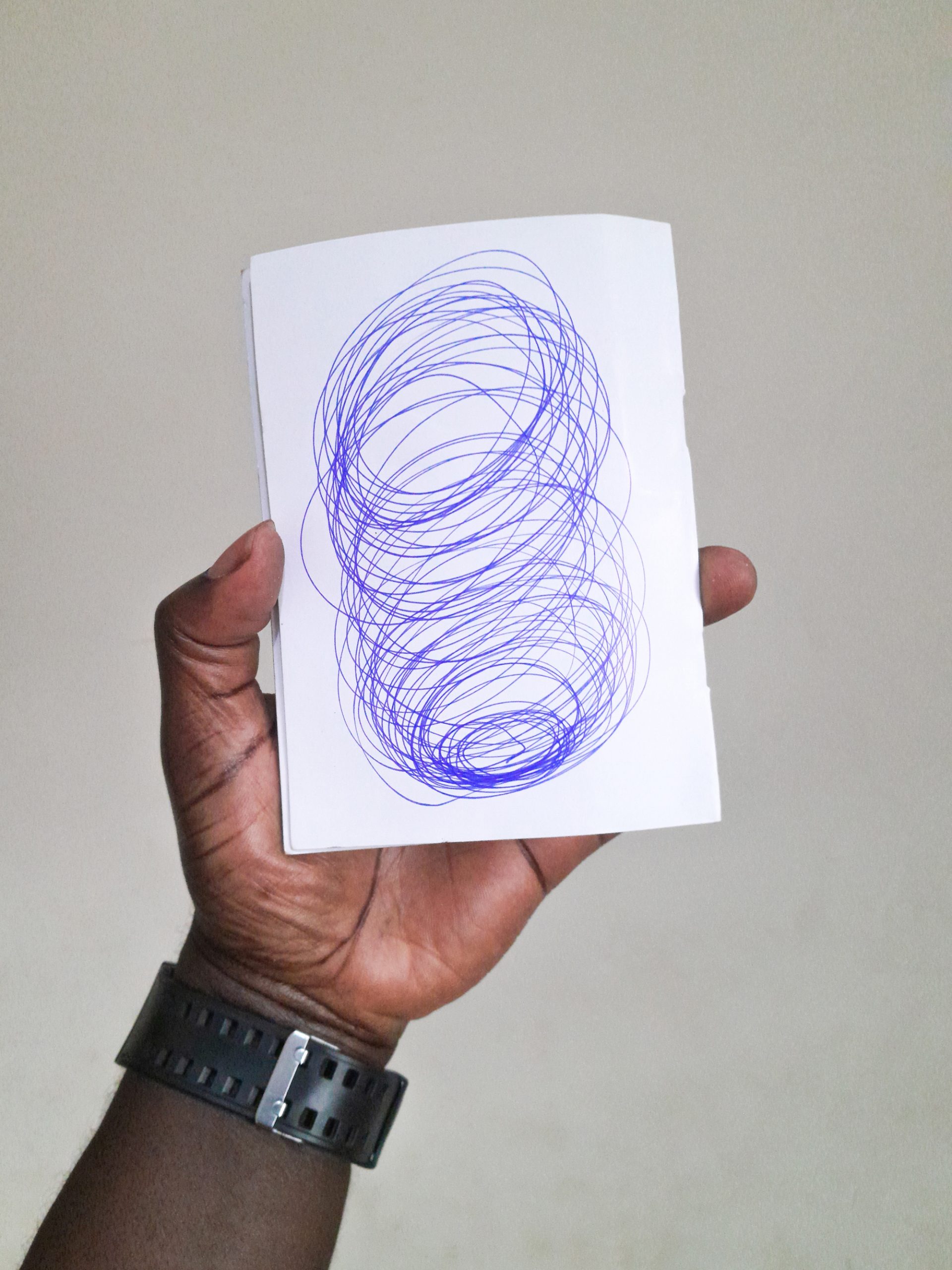 Overlapping outlines of circles in blue ink almost fill a blank white piece of paper held by a person with a black hand