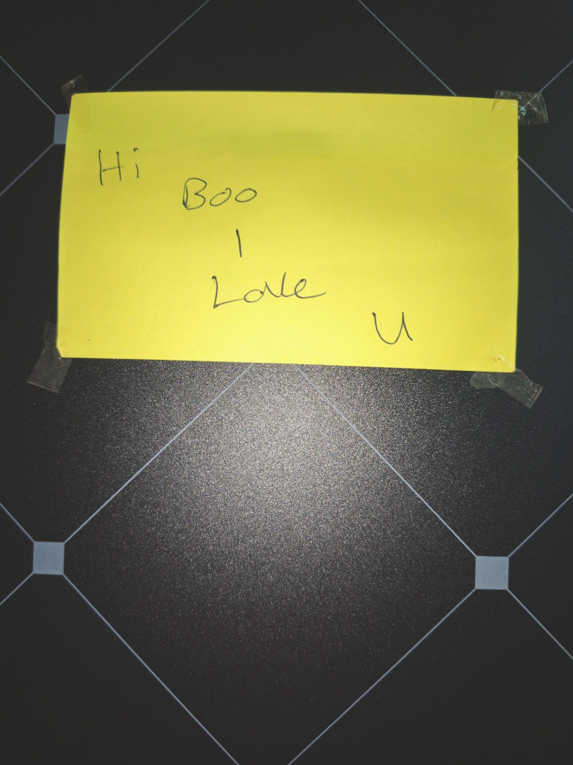 A yellow note resting on square tiles reads: "Hi Boo I love you"