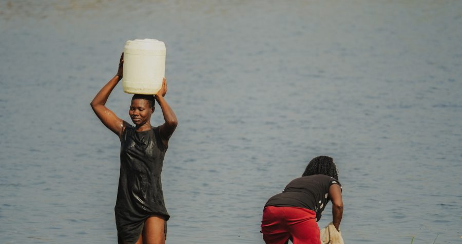 Two women by a lake are filling vessels up with water