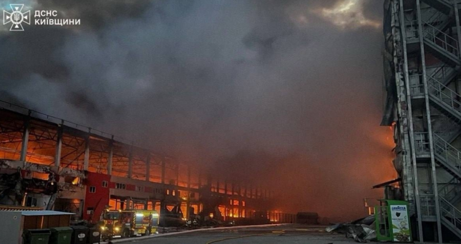 Smoke is coming out of a warehouse burning, and fire is burning down the walls.