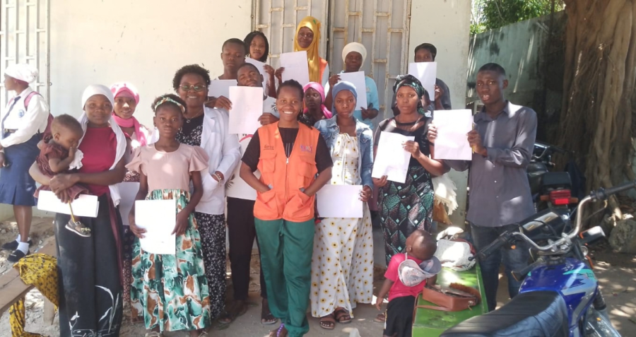 A young peer supporter stands outside a building in the middle of a group of people holding certificates